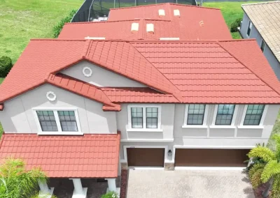 residential-roofing-02 - Linear Roofing - A Stronghouse Partner Aerial view of a two-story house with red tile roof, gray exterior, and a double garage; palm trees and a screened pool enclosure visible in the yard behind the house.