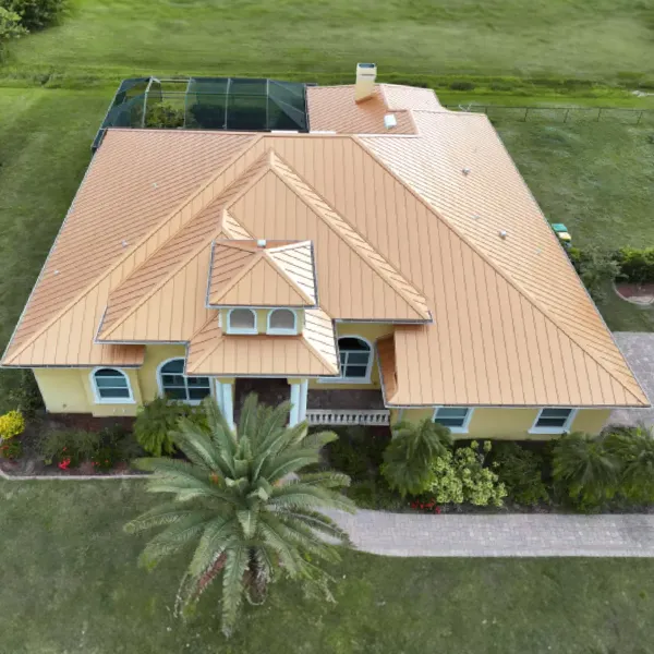specialty-hero - Linear Roofing - A Stronghouse Partner Aerial view of a yellow single-story house with an orange tile roof, palm trees in the front yard, a paved walkway, and a screened pool enclosure at the back.